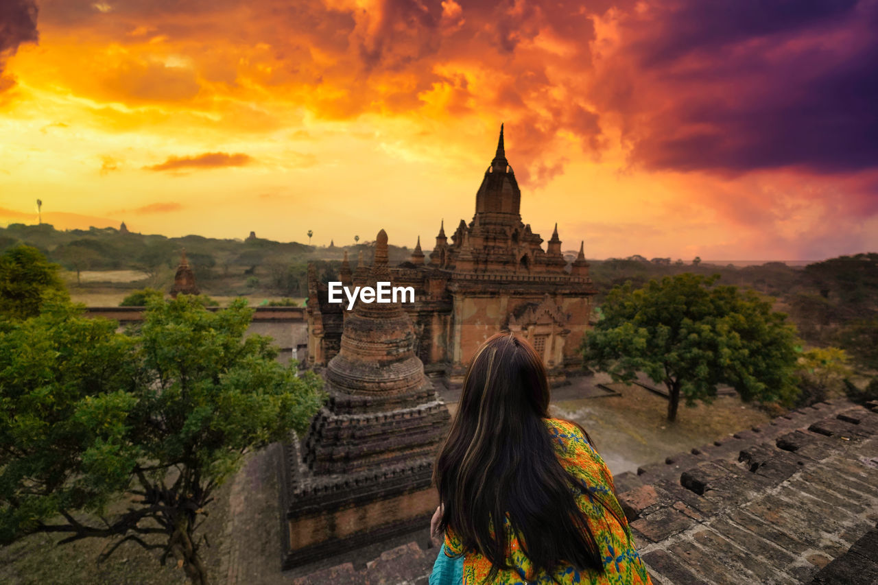 Rear view of woman sitting at temple against sky during sunset