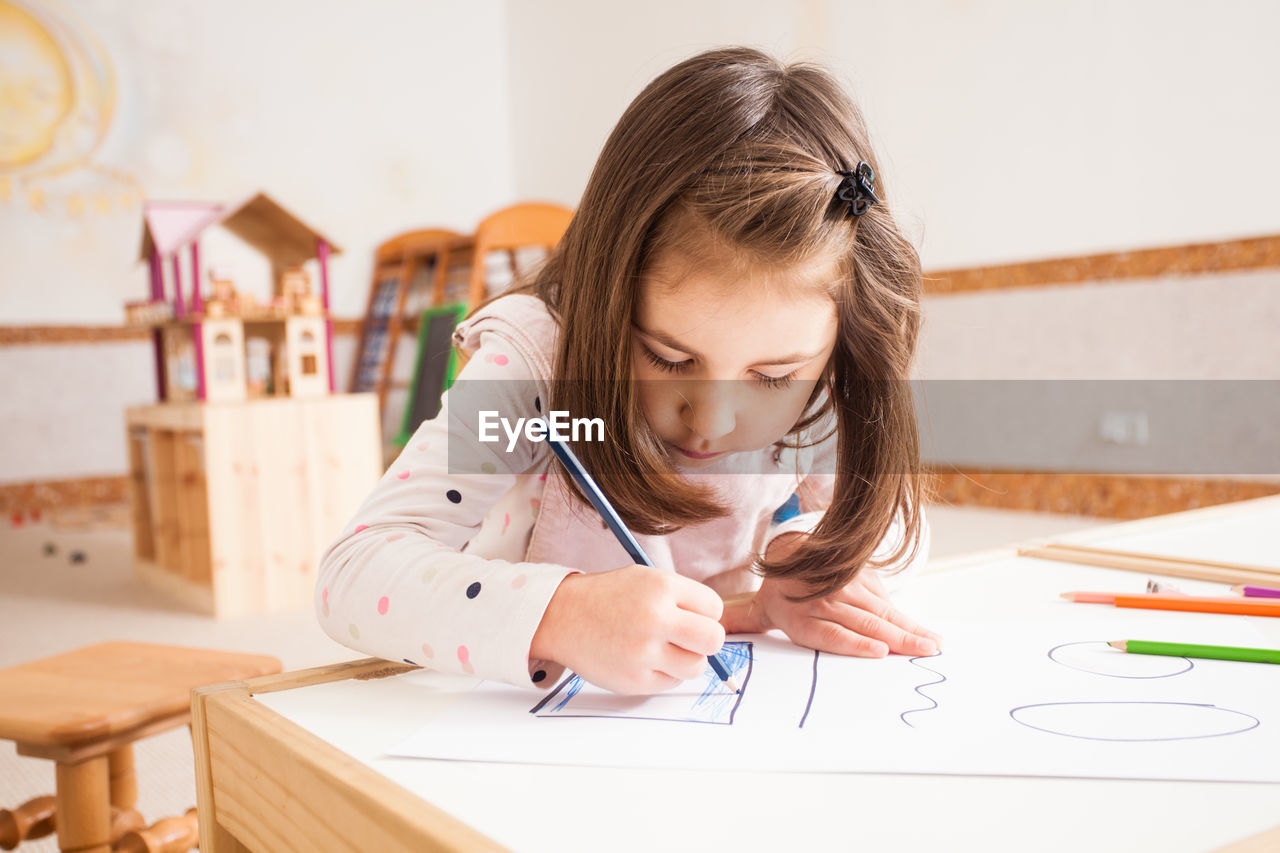 Portrait of girl holding table against wall