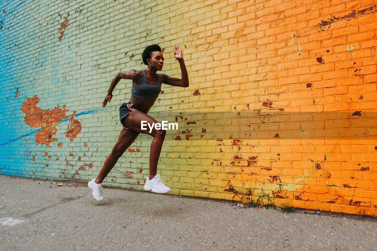 Woman running on road against brick wall in city