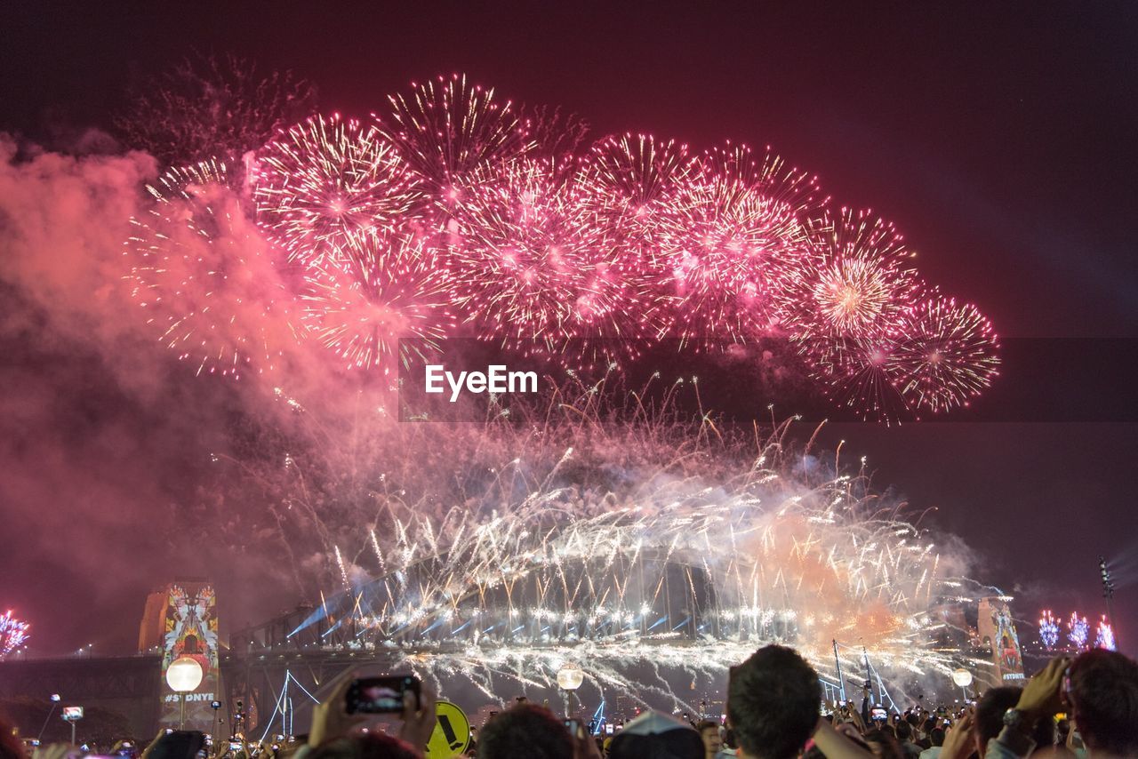 Rear view of people looking at fireworks display against sky at night