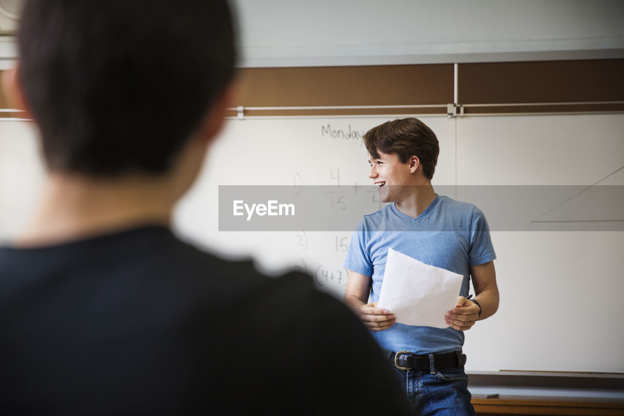 Man holding paper while standing against whiteboard in classroom