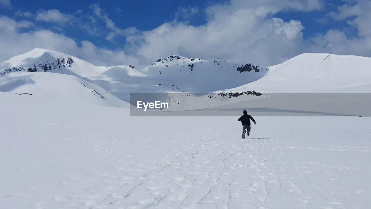 Rear view of man running towards snowcapped mountains against sky