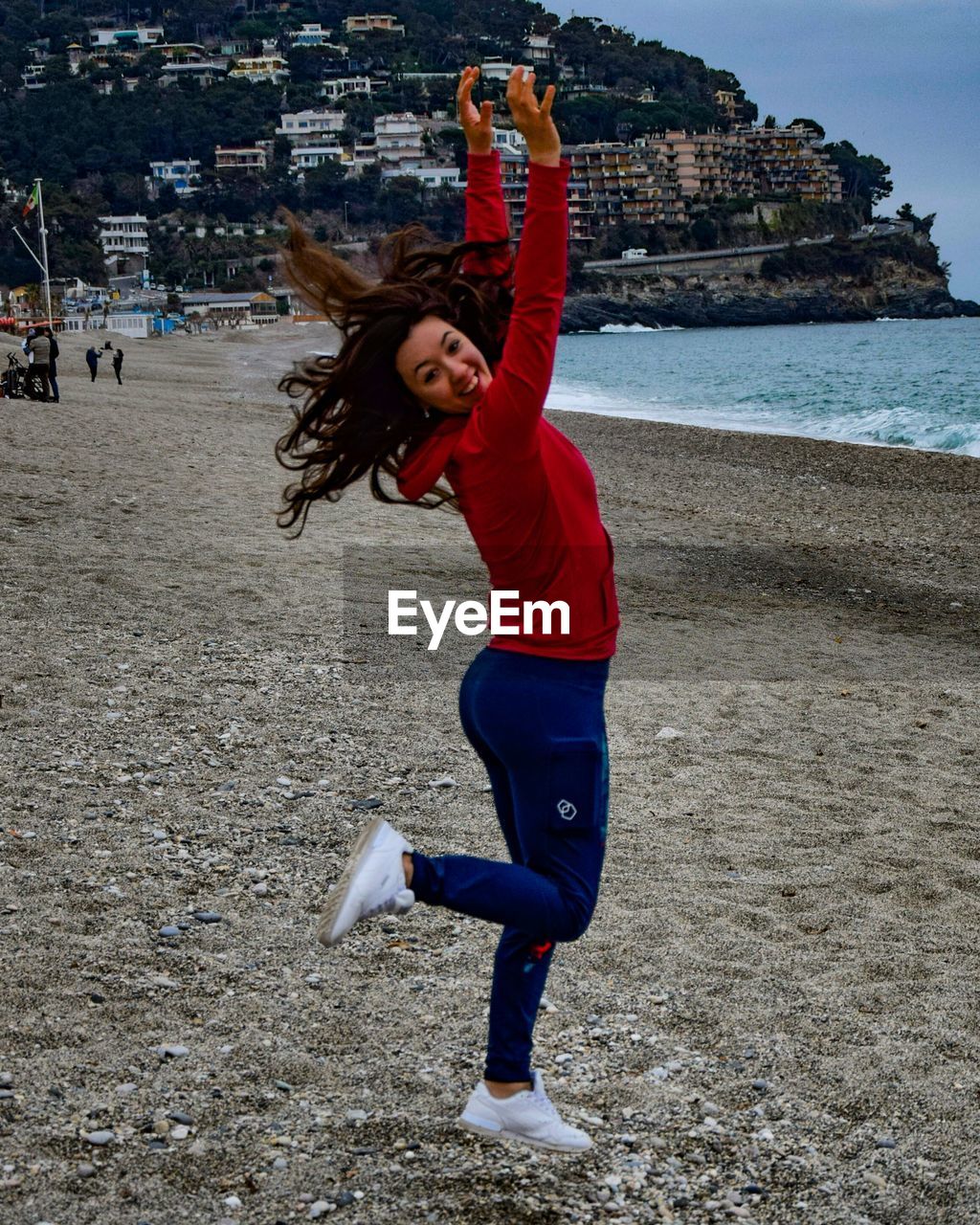 Portrait of happy young woman with arms raised jumping at beach