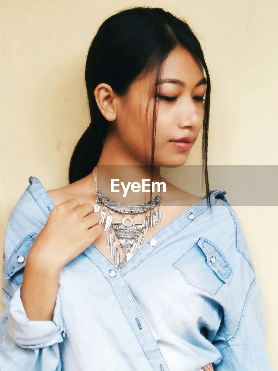 Young woman wearing necklace while standing against wall