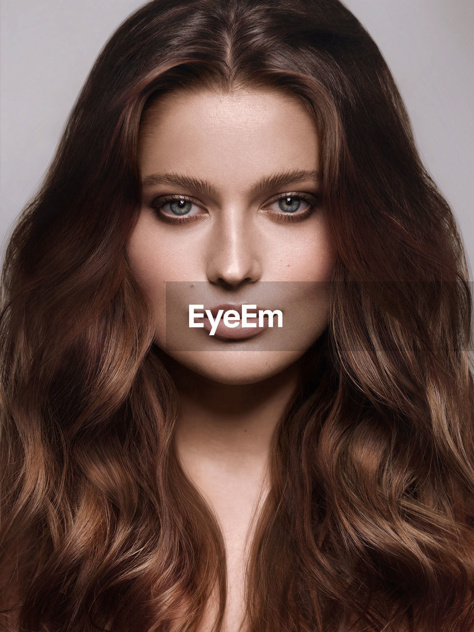 Close-up portrait of beautiful young woman with brown hair over white background