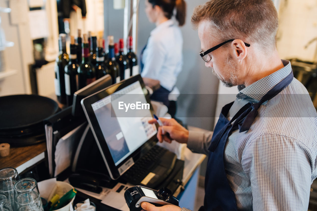 Owner using computer while holding credit card reader in restaurant