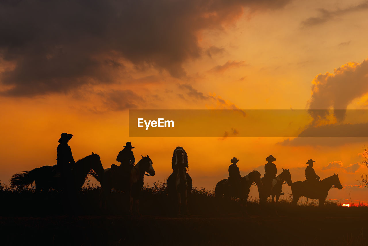 Group cowboy on horse silhouetted against a large sky