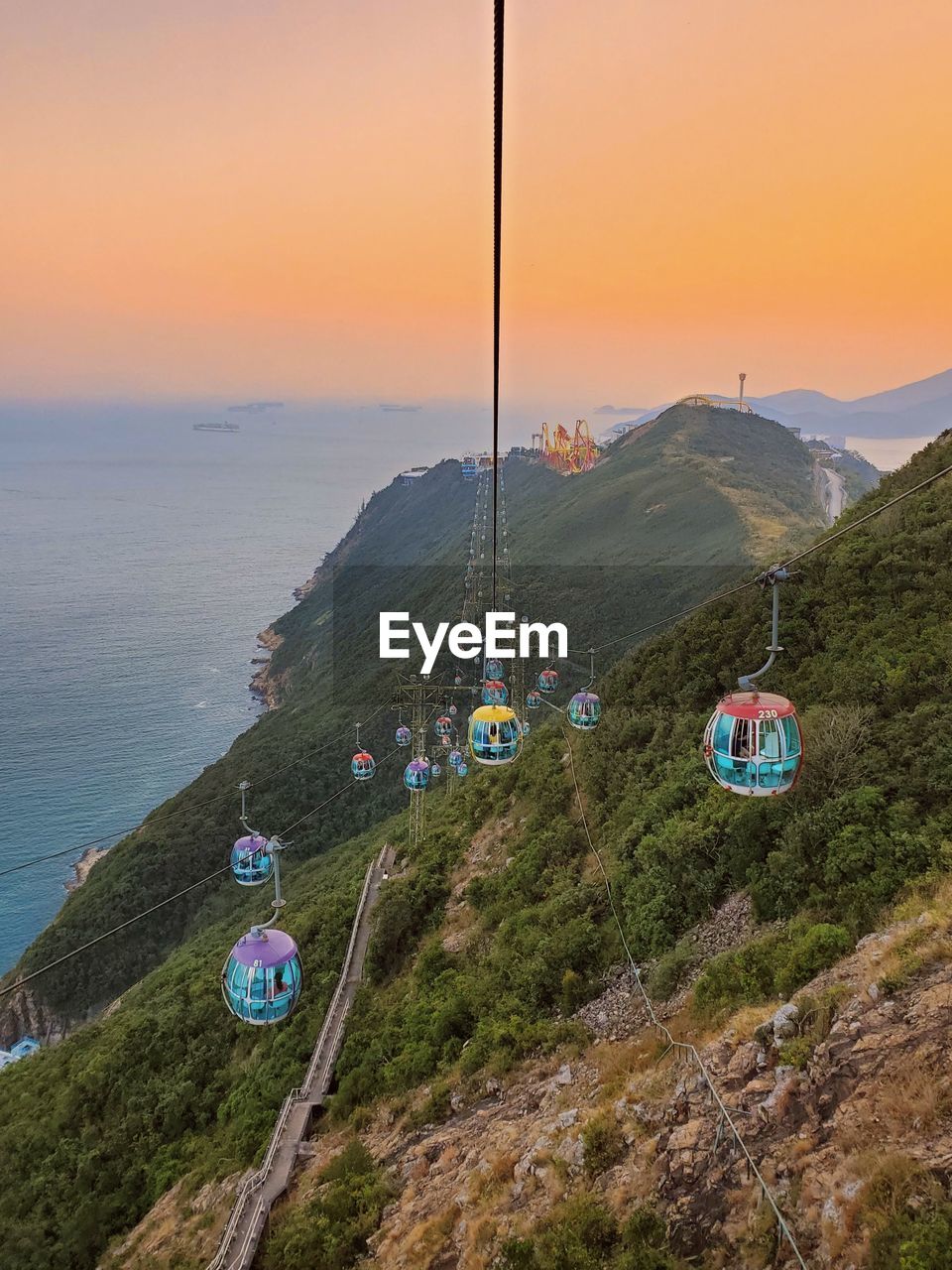 OVERHEAD CABLE CAR ON SEA BY MOUNTAINS AGAINST SKY