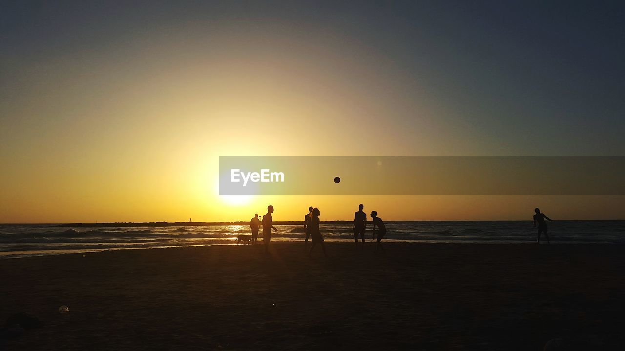 Silhouette friends playing with ball at beach against sky during sunset