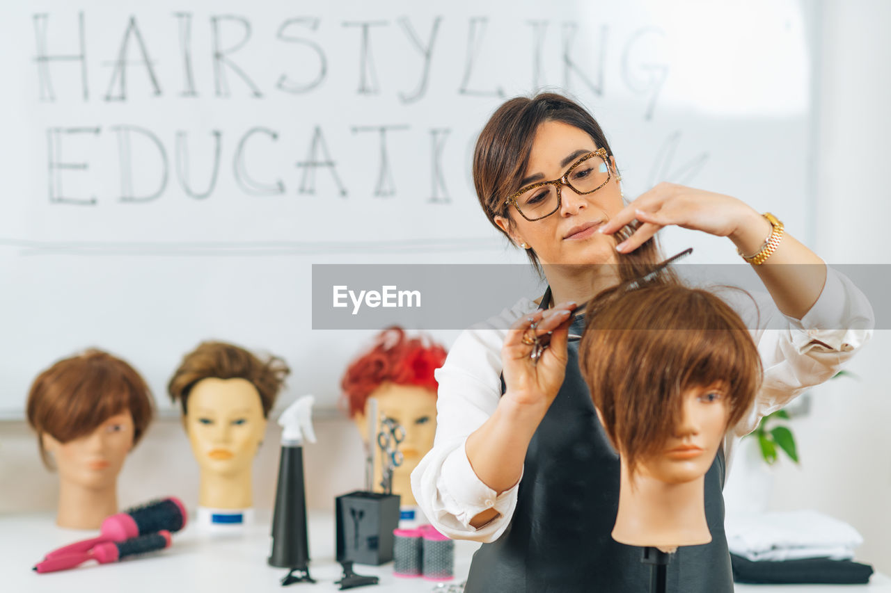 Hairdresser educator with students, explaining hair cutting technique on mannequin head for training