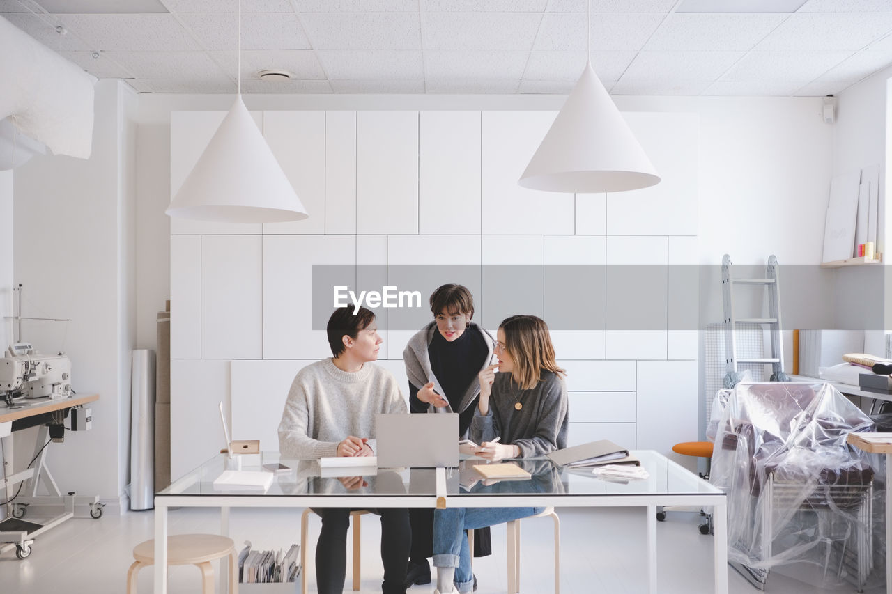 Female fashion designers discussing over laptop at desk in studio