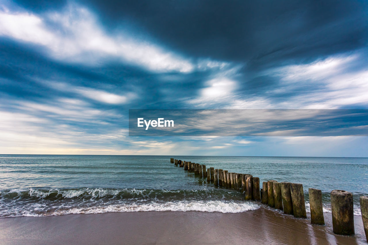 WOODEN POSTS ON SEA AGAINST SKY