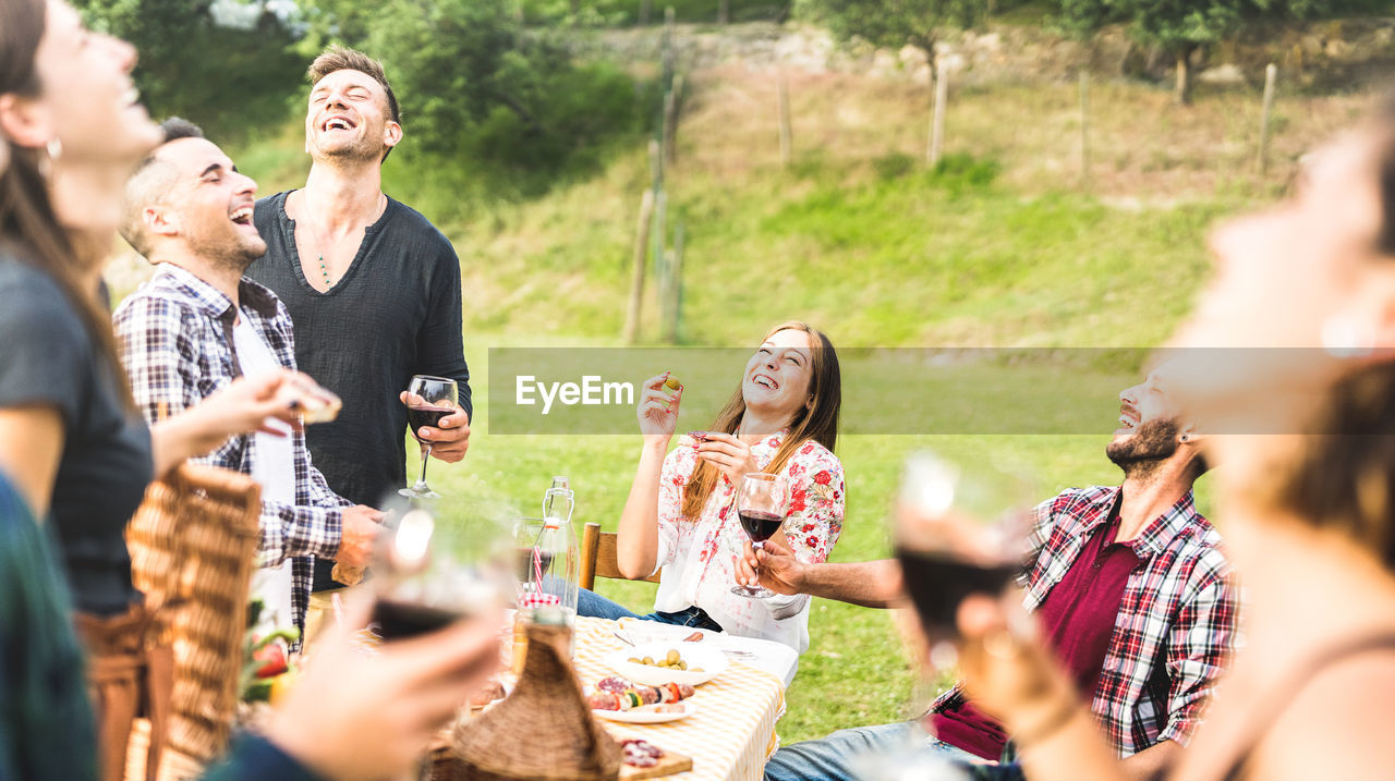 Friends laughing while having wine at park during picnic