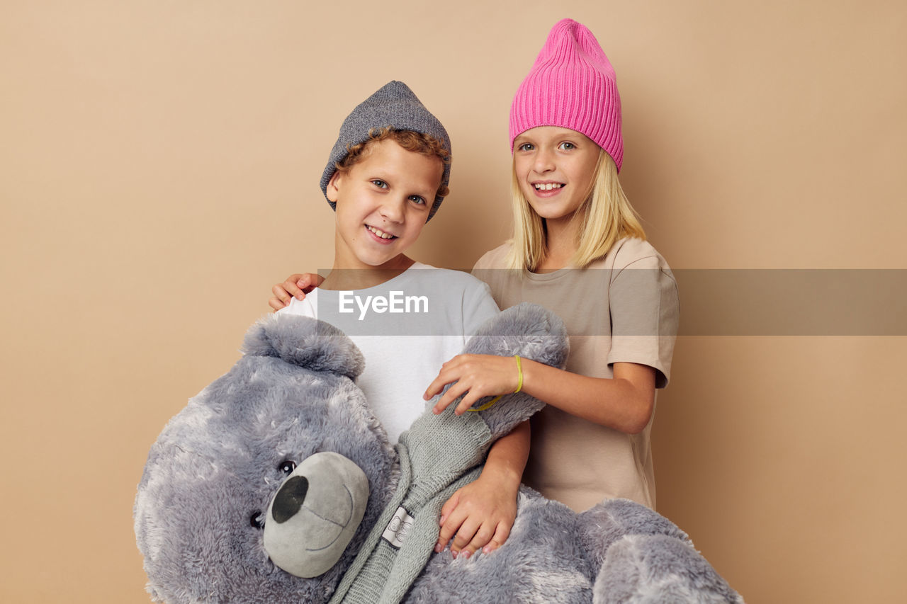 Portrait of sibling holding stuffed toy against beige background