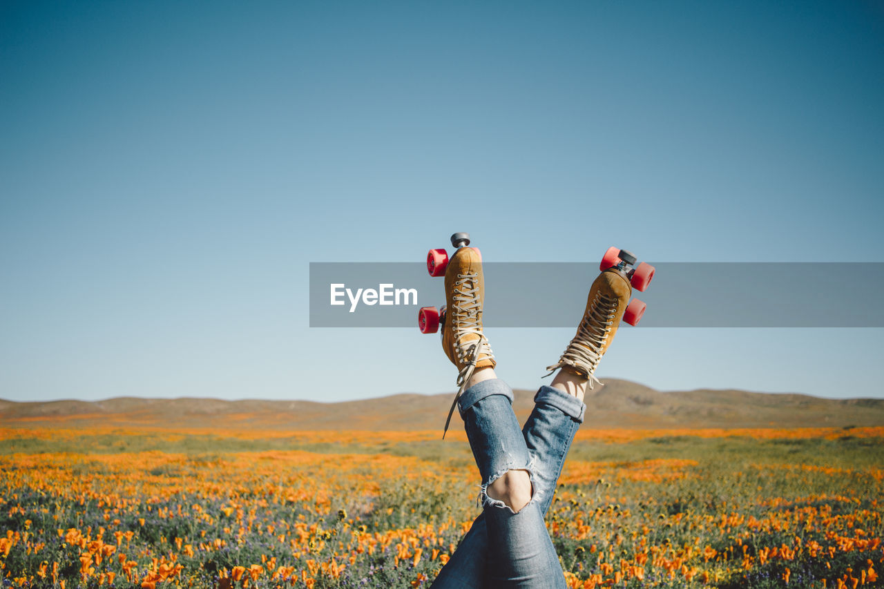 Low section of person with roller skates on landscape against clear blue sky