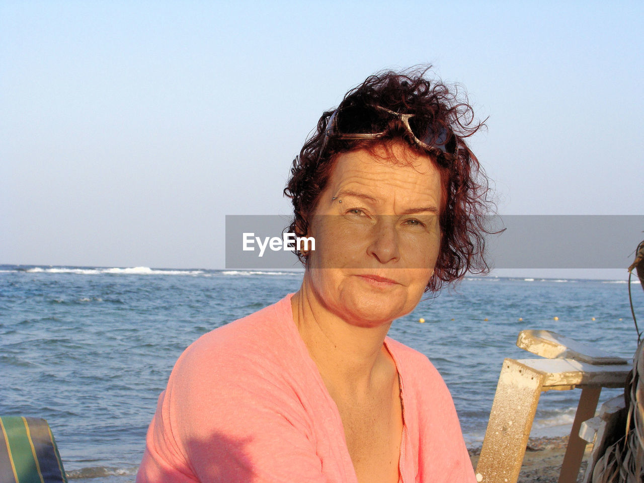 Mature woman sitting at beach against clear sky