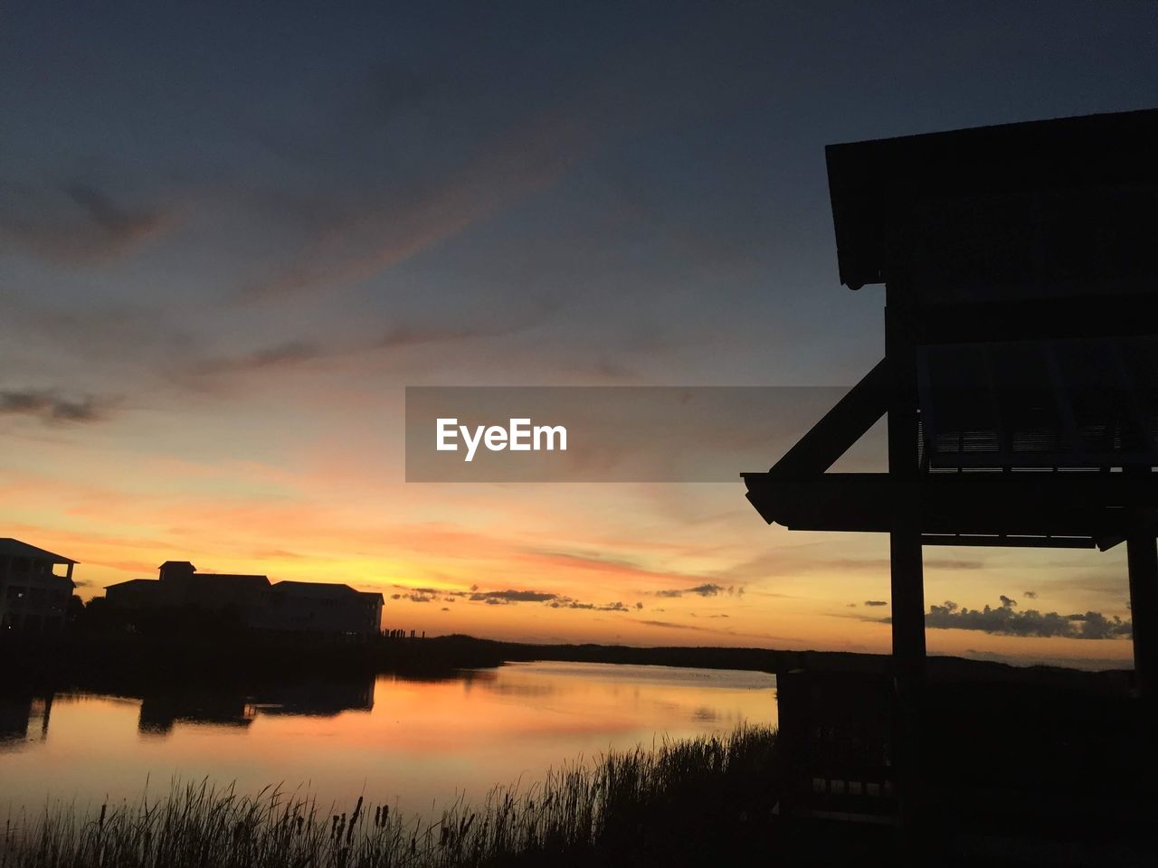 SILHOUETTE BUILDINGS BY LAKE AGAINST ORANGE SKY