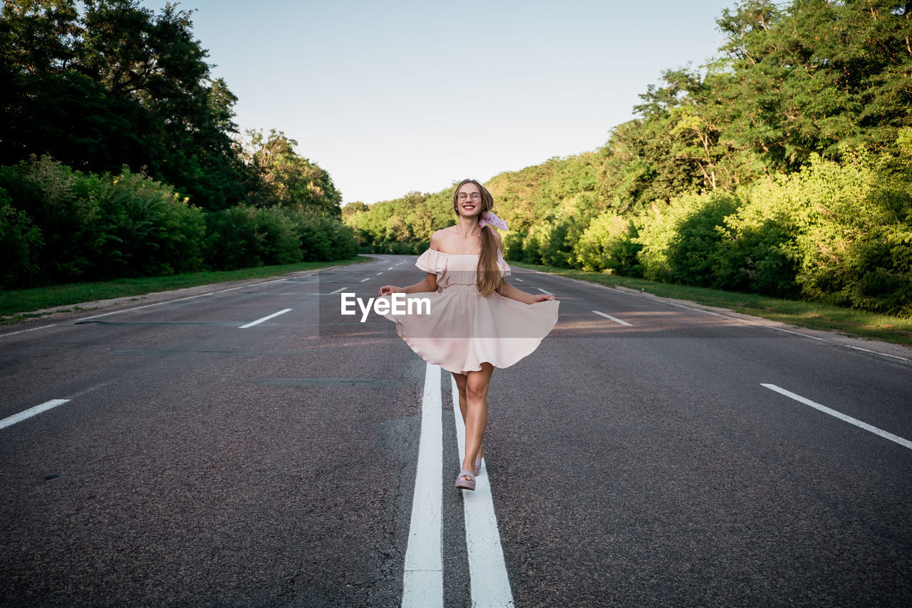 Portrait of woman standing on road against trees