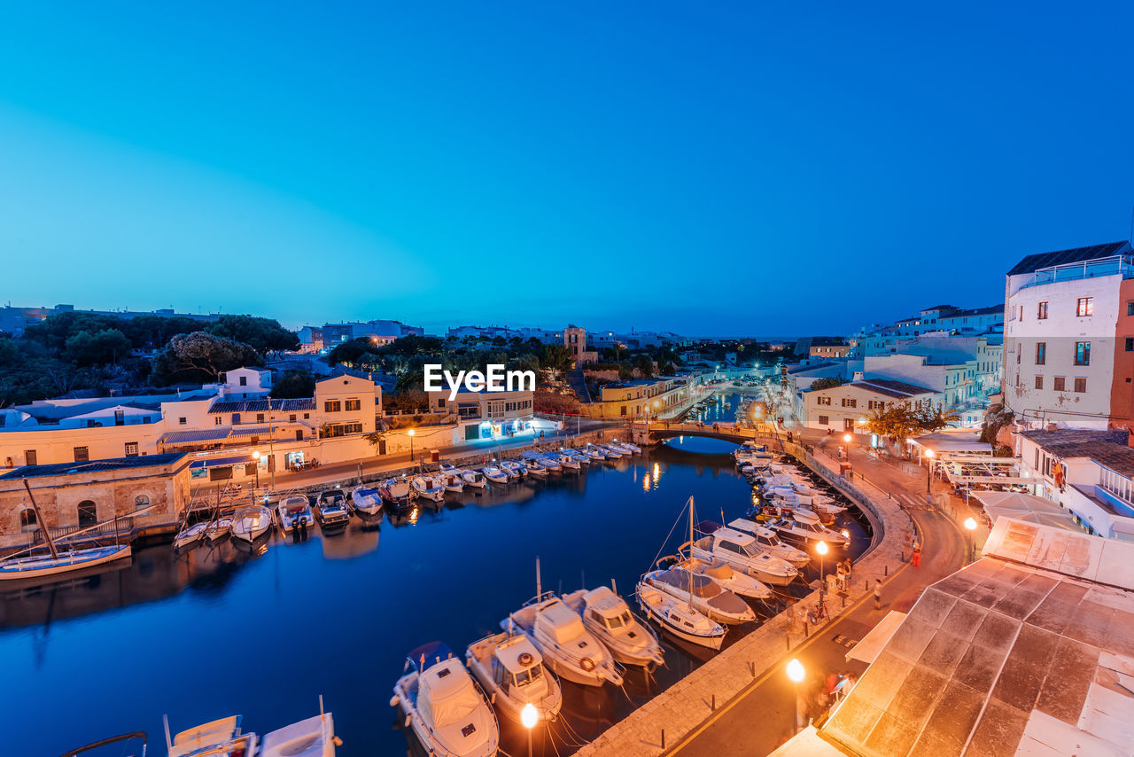 High angle view of illuminated buildings by river against blue sky