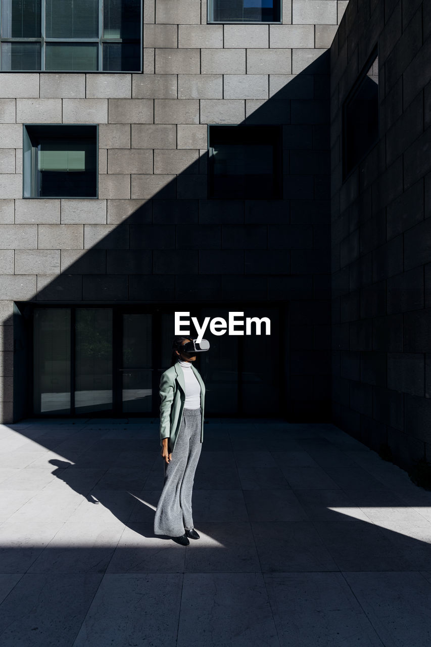 Businesswoman using vr goggles by office building on sunny day