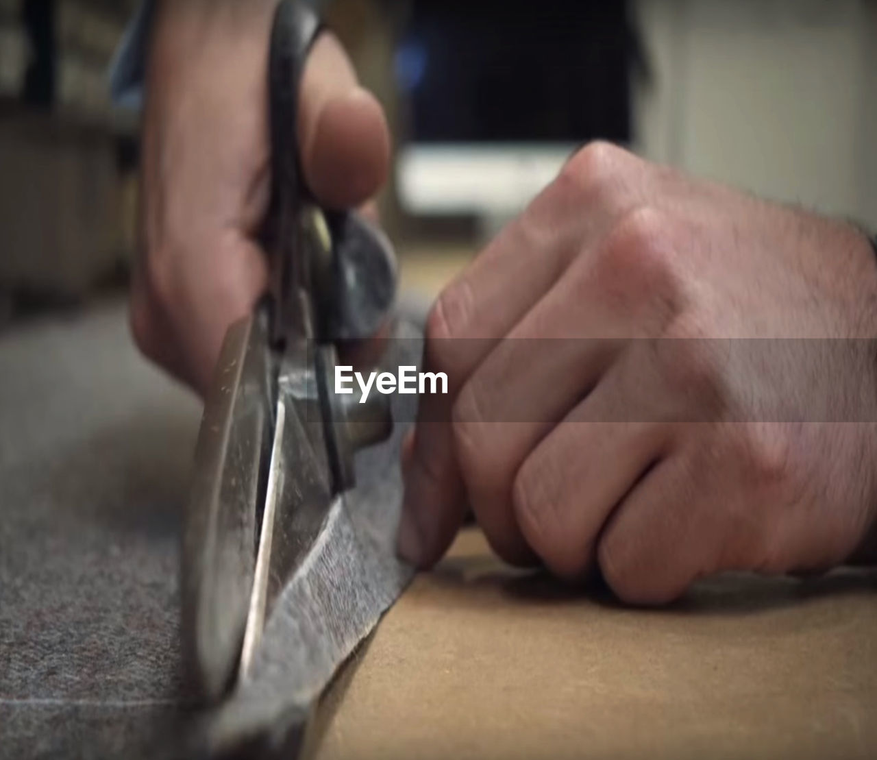 Close-up of hands using scissors to cut textile at workshop