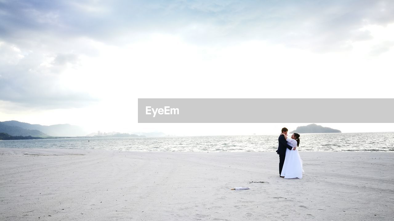 REAR VIEW OF COUPLE ON BEACH AGAINST SKY