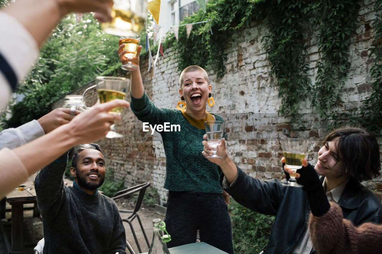 Cheerful woman with mouth open toasting drinks with friends during dinner party in back yard