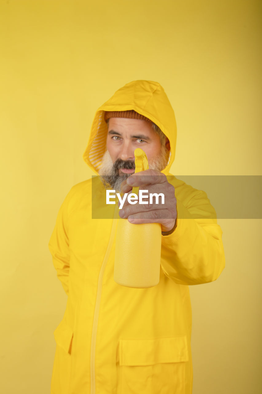 Handsome man holding a washing spray in a yellow raincoat standing behind a yellow wall person