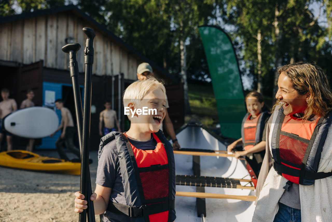 Happy boy with counselor wearing life jackets while going for kayaking at summer camp