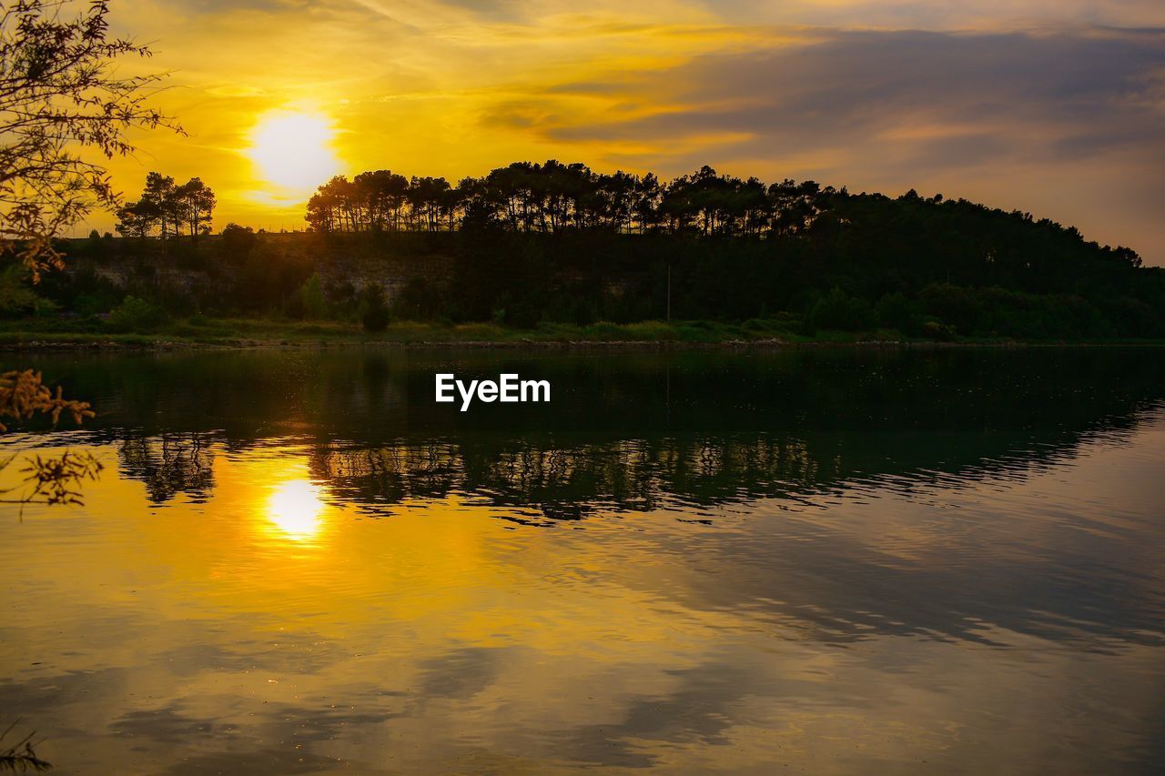 SCENIC VIEW OF LAKE BY SILHOUETTE TREES AGAINST SKY AT SUNSET