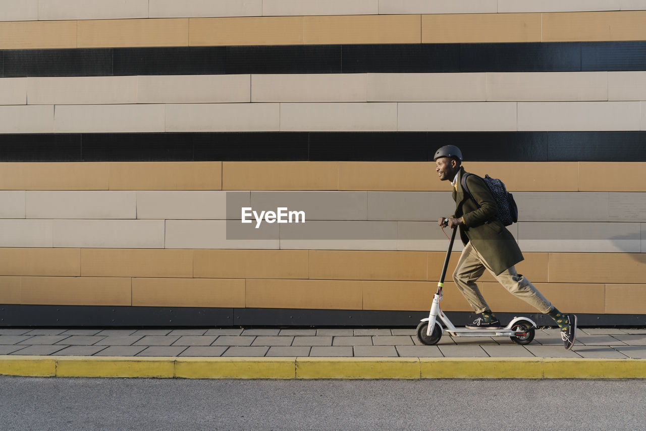 Stylish man with helmet and scooter passing a building