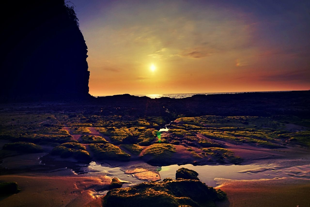 Rocks at beach against sky during sunset