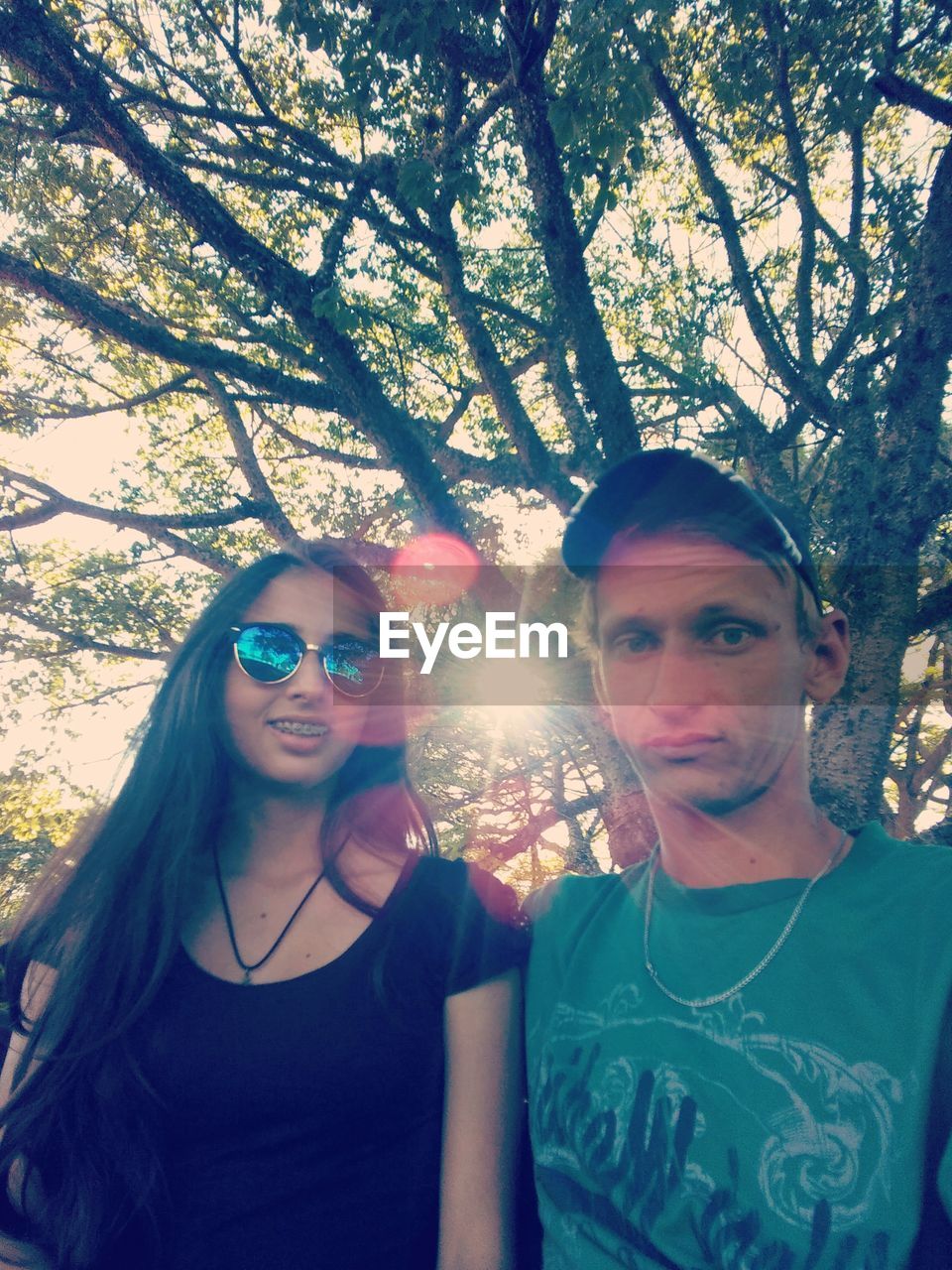 PORTRAIT OF SMILING YOUNG COUPLE STANDING AGAINST TREE