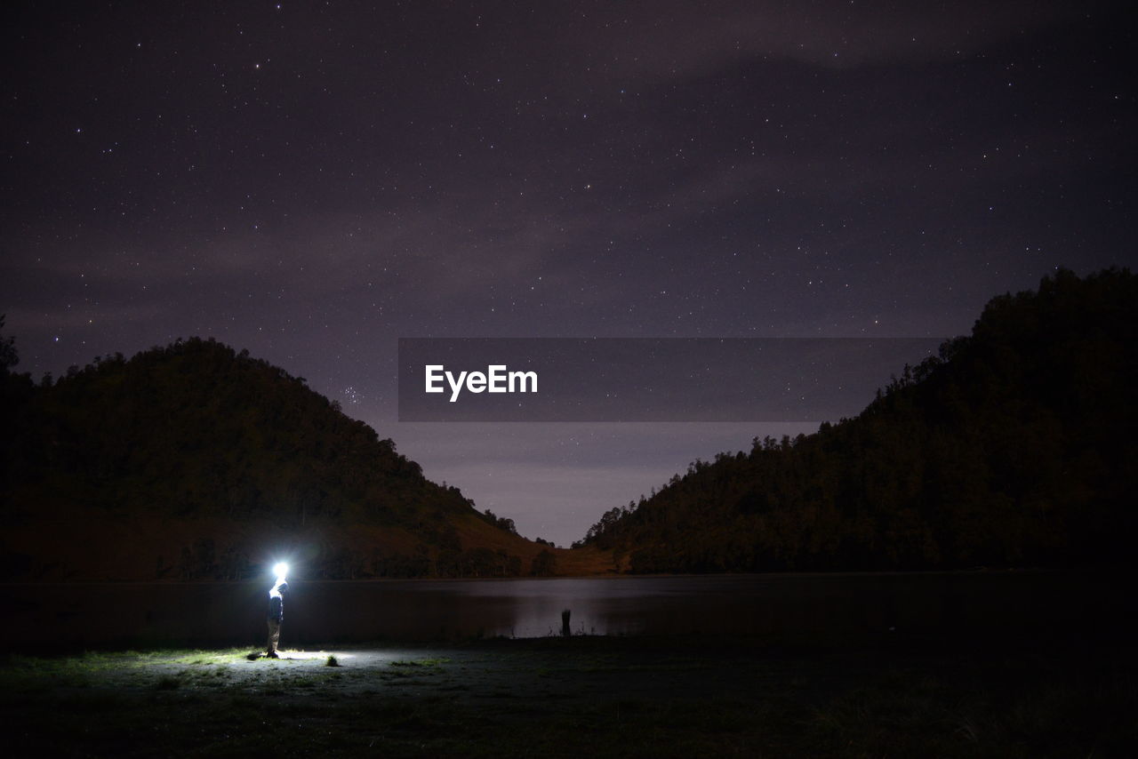 Silhouette trees by lake against sky at night