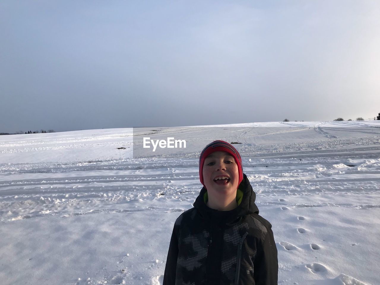 Portrait of smiling boy standing on snow covered landscape against sky during sunset