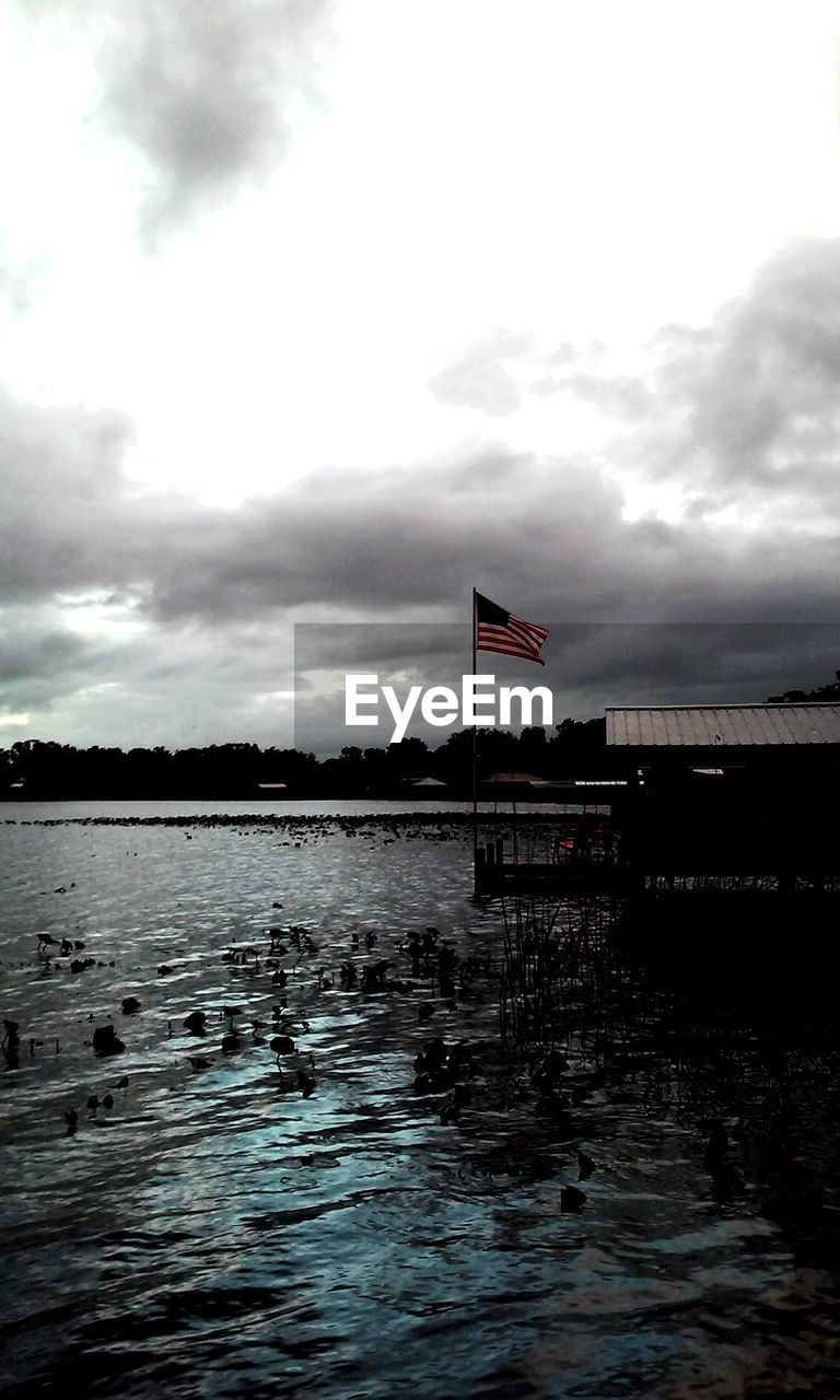 American flag by lake against cloudy sky