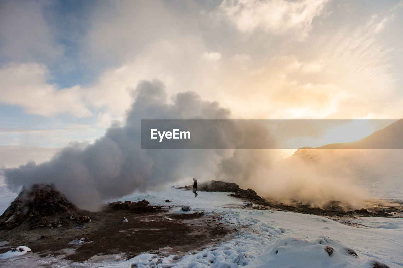 Unrecognizable explorer walking in highlands in winter near fuming volcano at sunset in iceland