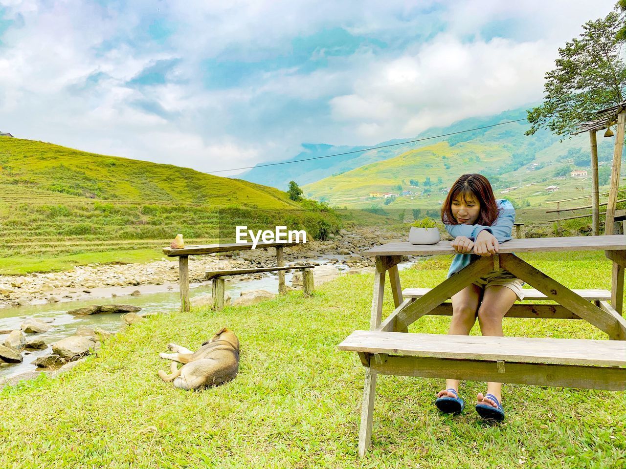 Woman sitting on grass against mountains