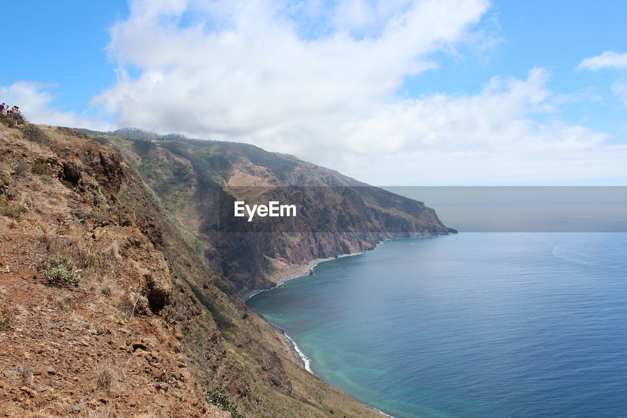 Scenic view of cliff and sea against cloudy sky