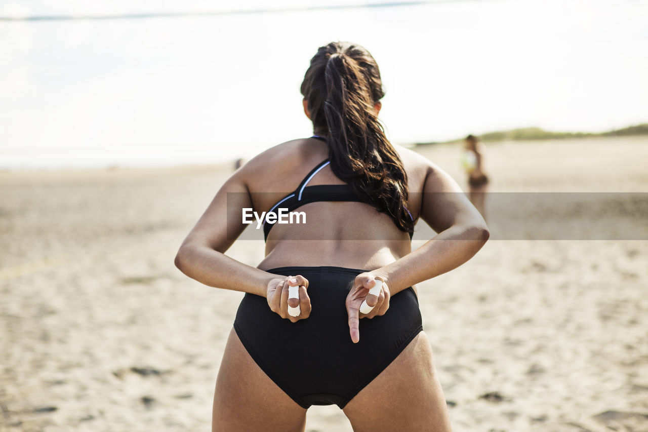 Rear view of woman standing at beach while playing volleyball