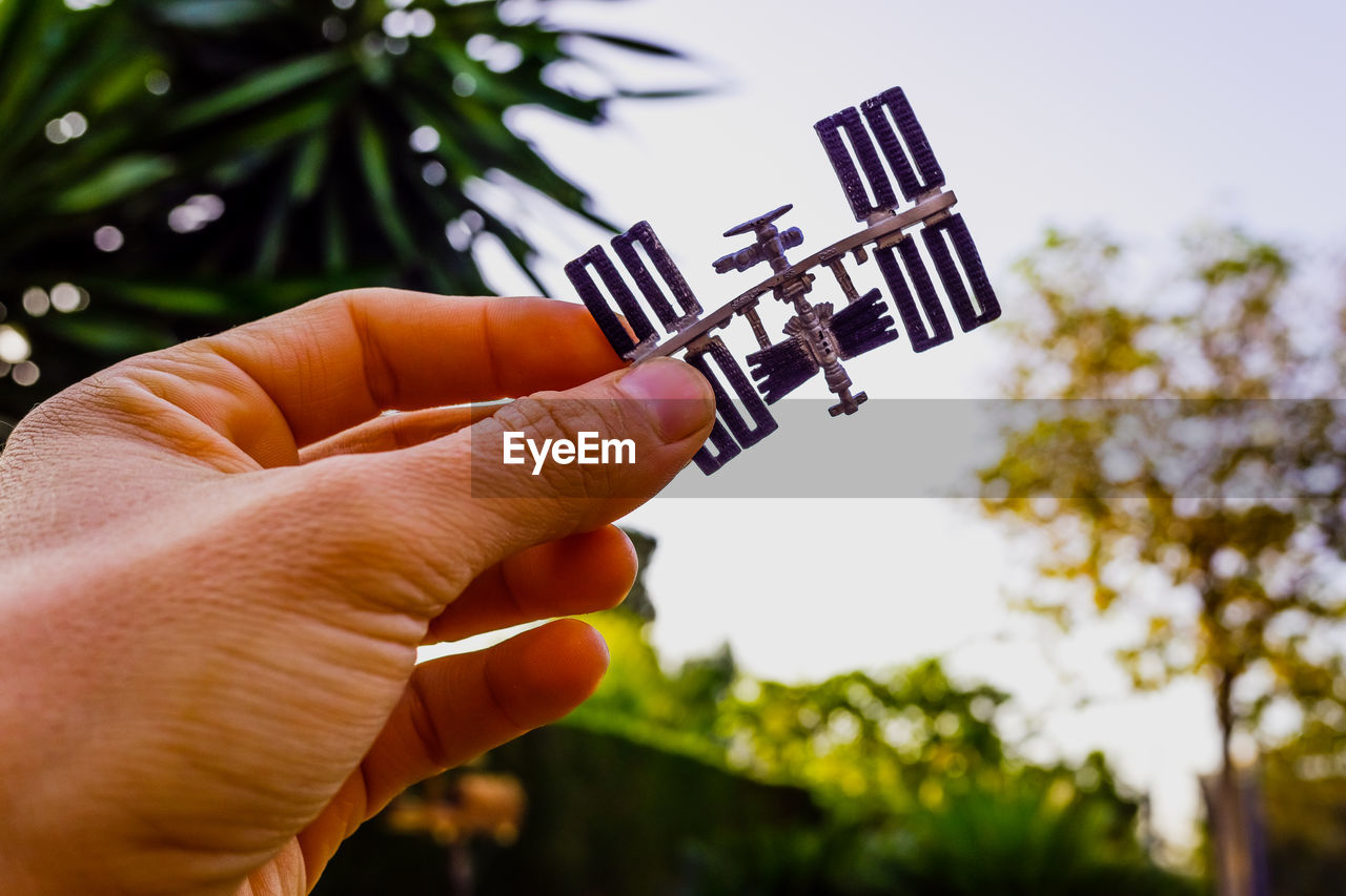 Close-up of hand holding model satellite against sky