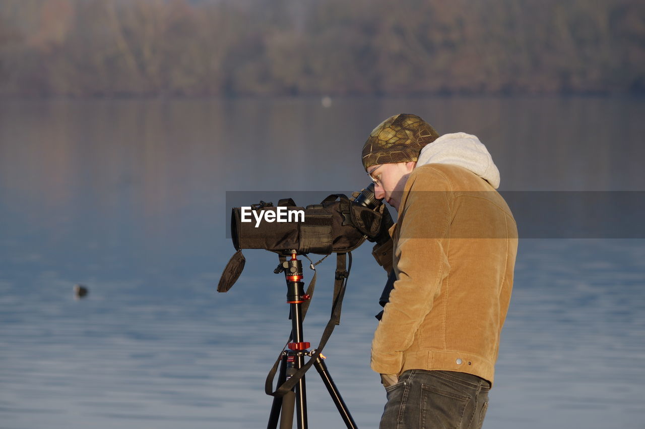 Side view of man photographing by lake