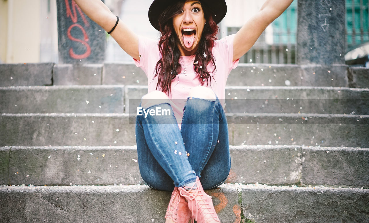 Portrait of excited woman sticking out tongue while sitting on steps