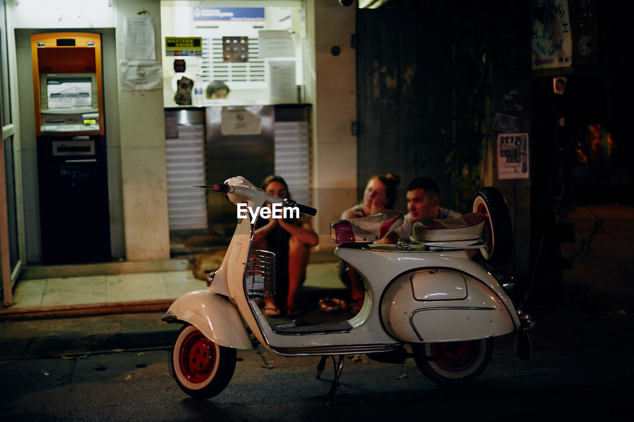 transportation, mode of transportation, adult, vehicle, men, scooter, city, group of people, architecture, women, full length, sitting, vespa, street, night, travel, land vehicle, leisure activity, lifestyles