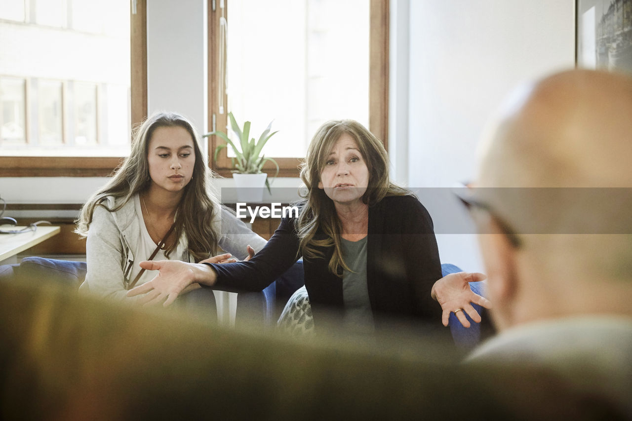 Mother sitting with daughter while sharing problems to male therapist at community center