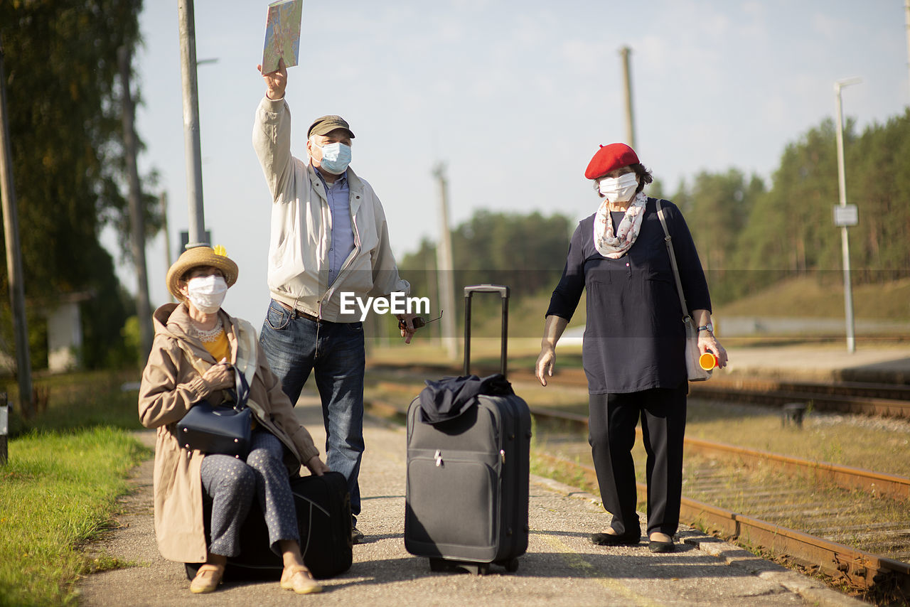 Positive elderly seniors people with face masks waiting train before traveling during a pandemic