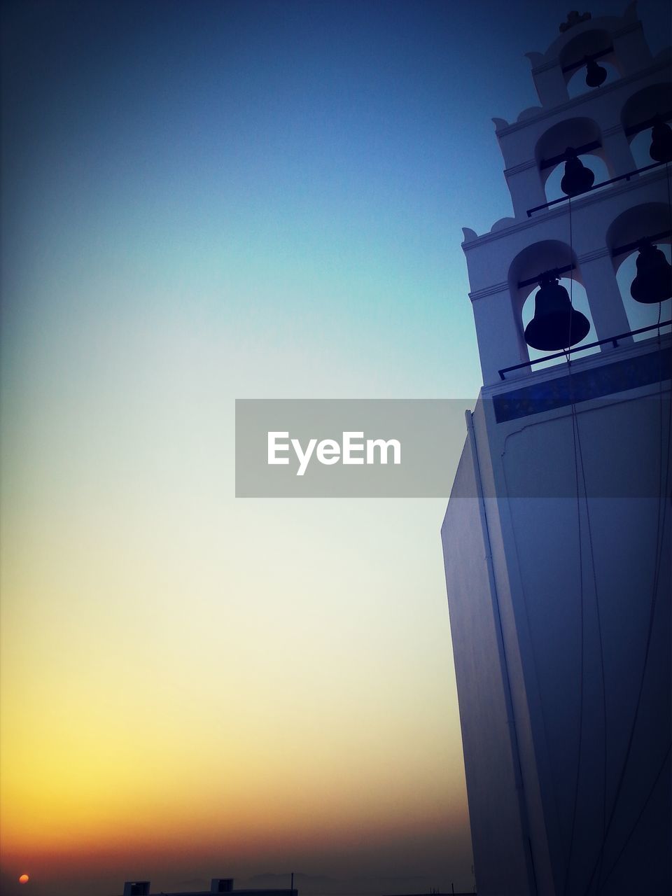 Low angle view of bell tower against sky during sunset at oia