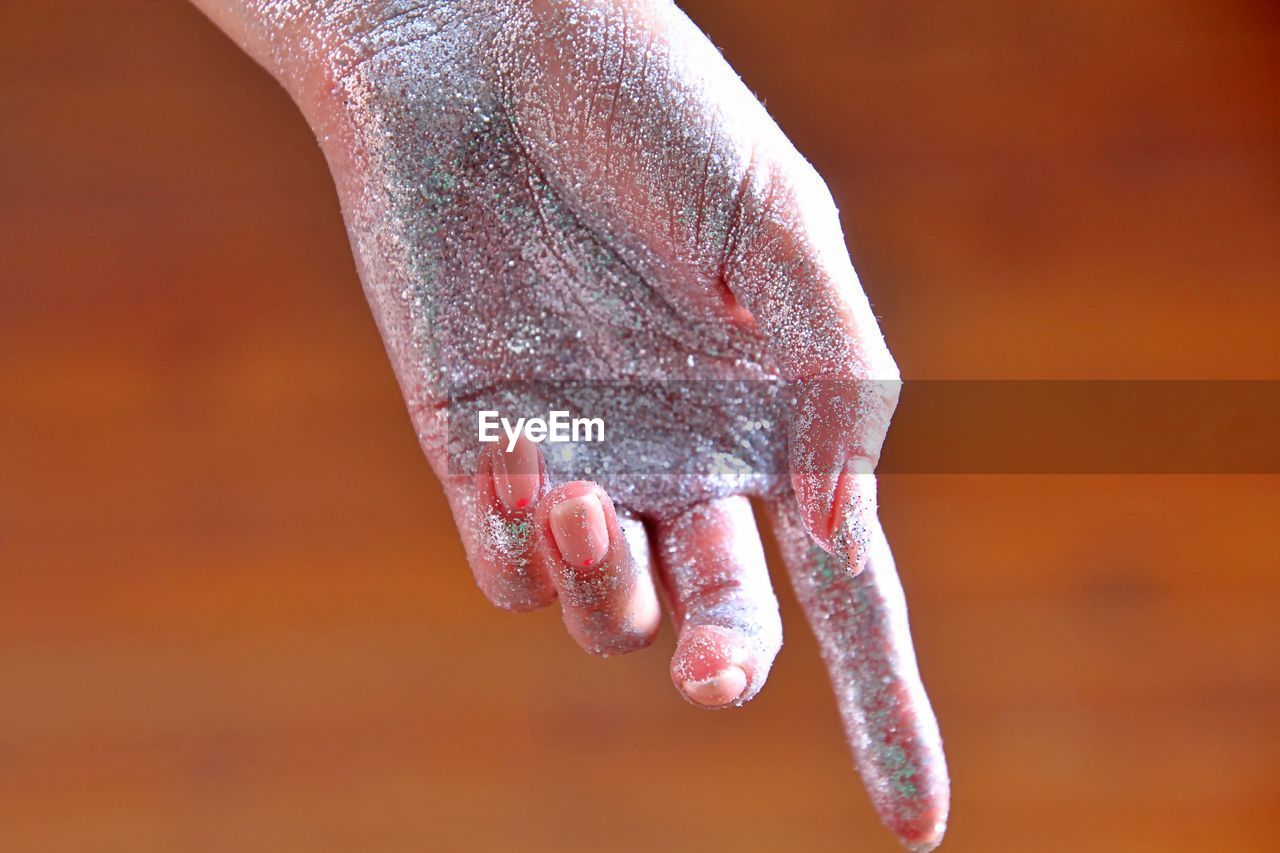 Cropped hand of woman with glitter against orange background