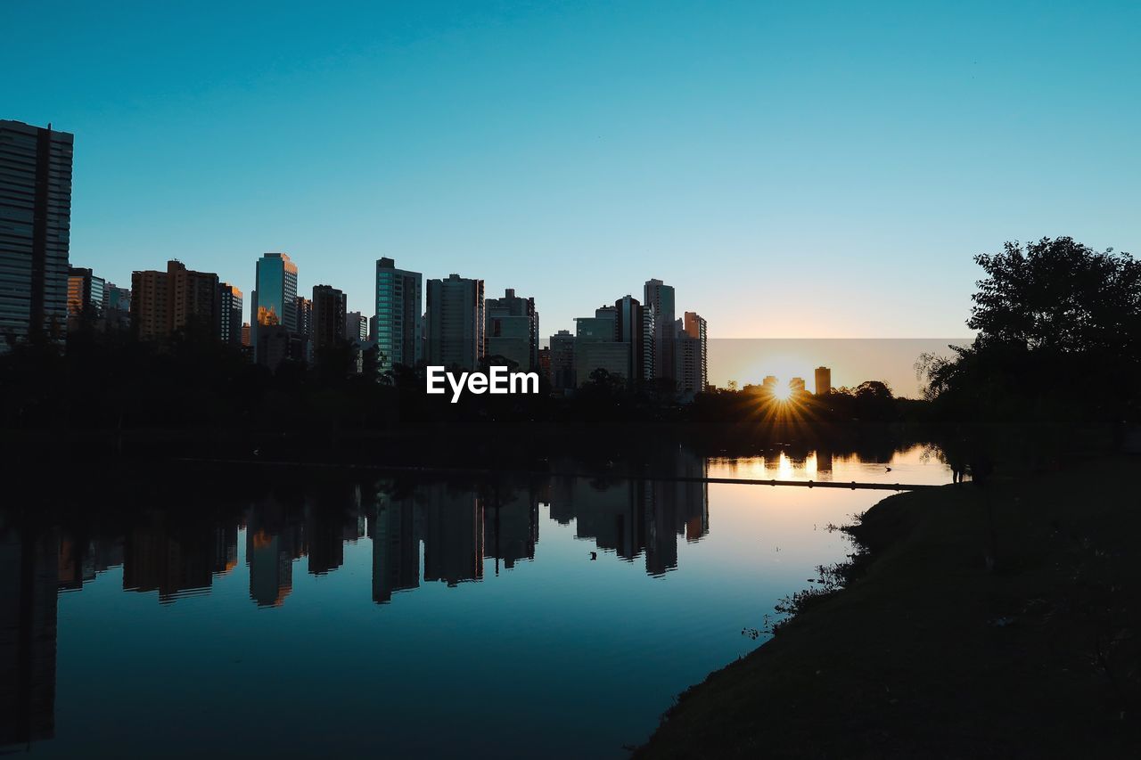 Reflection of silhouette trees and buildings against sky during sunset