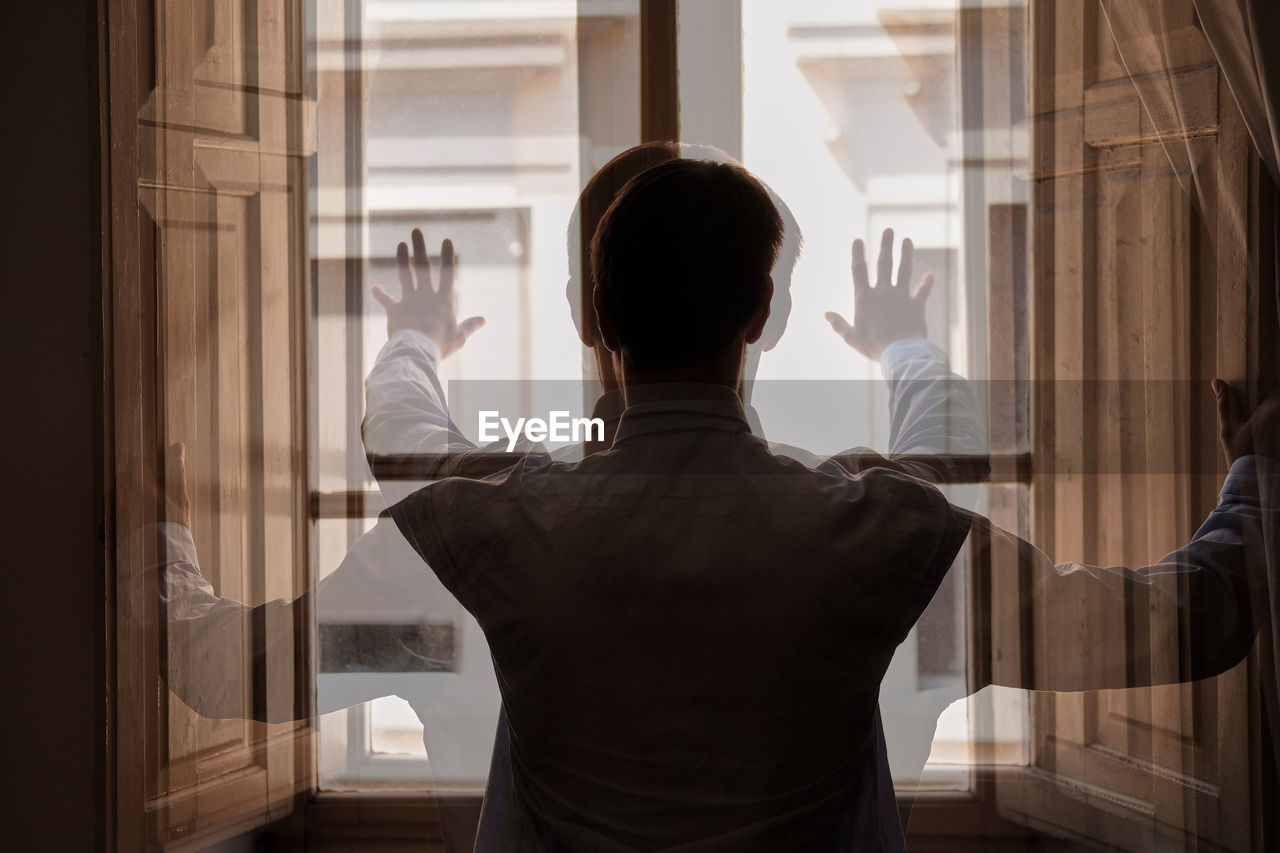 Double exposure of man looking through window at home